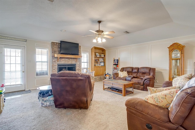 carpeted living room with visible vents, lofted ceiling, ceiling fan, a brick fireplace, and a decorative wall