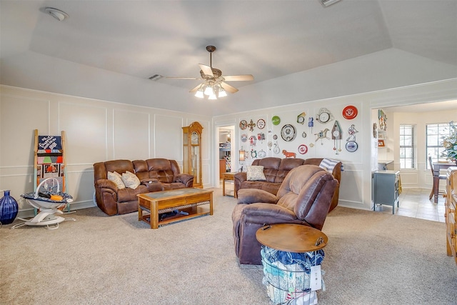 carpeted living room featuring ceiling fan, vaulted ceiling, visible vents, and a decorative wall