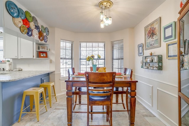 dining room featuring a wainscoted wall, a decorative wall, and light tile patterned flooring