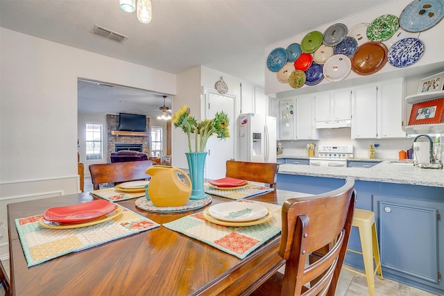 dining space with a large fireplace, visible vents, and ceiling fan