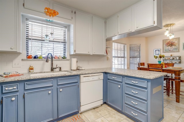 kitchen featuring white dishwasher, a peninsula, a sink, blue cabinetry, and backsplash