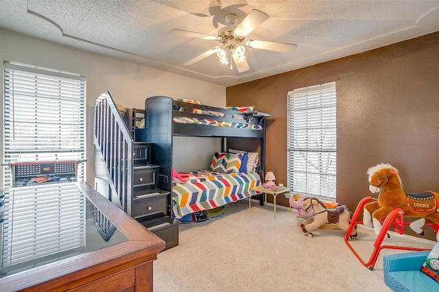 carpeted bedroom featuring a textured wall, multiple windows, ceiling fan, and a textured ceiling