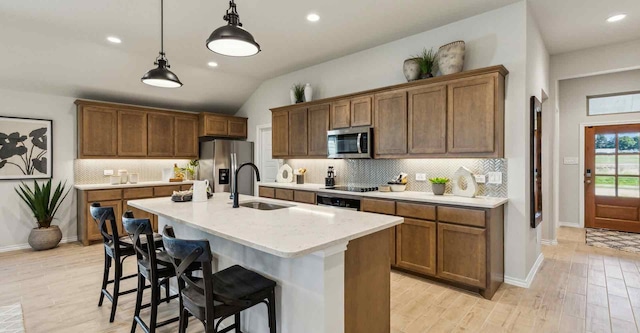 kitchen featuring a kitchen breakfast bar, a kitchen island with sink, stainless steel appliances, light countertops, and a sink