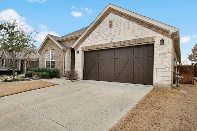 view of front of property with an attached garage, stone siding, fence, and concrete driveway