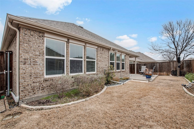 back of property with a patio area, roof with shingles, fence, and brick siding