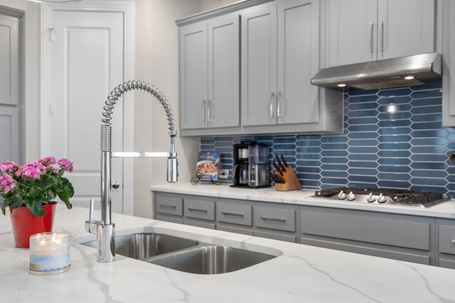 kitchen featuring stainless steel gas cooktop, gray cabinets, decorative backsplash, a sink, and under cabinet range hood