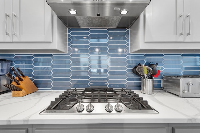 kitchen featuring a toaster, extractor fan, stainless steel gas stovetop, white cabinetry, and backsplash