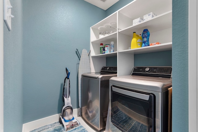 clothes washing area with laundry area, a textured wall, baseboards, and separate washer and dryer