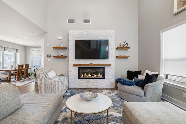 living area featuring a towering ceiling, a glass covered fireplace, wood finished floors, and visible vents