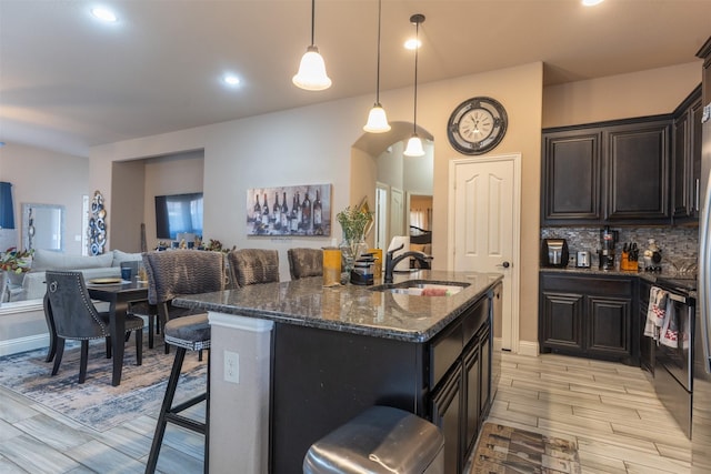 kitchen featuring a breakfast bar area, a sink, backsplash, dark stone counters, and a center island with sink