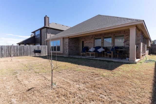 back of house with brick siding, a yard, a patio, a shingled roof, and fence