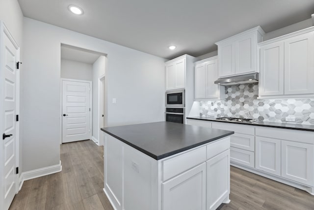 kitchen featuring appliances with stainless steel finishes, dark countertops, light wood-type flooring, and under cabinet range hood