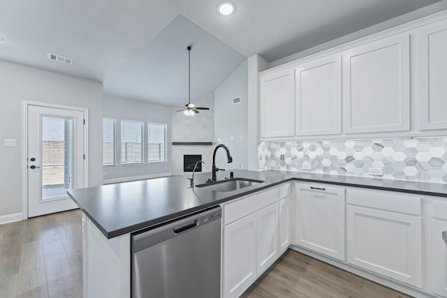 kitchen with dishwasher, dark countertops, a sink, and visible vents