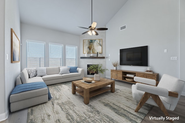 living room with a warm lit fireplace, a ceiling fan, visible vents, and wood finished floors