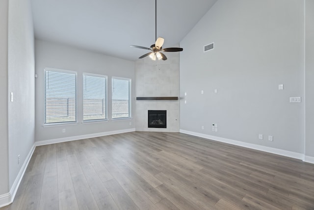 unfurnished living room with a tile fireplace, wood finished floors, visible vents, baseboards, and a ceiling fan