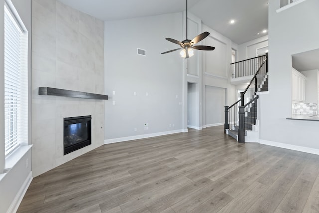 unfurnished living room with visible vents, a towering ceiling, wood finished floors, a tile fireplace, and stairs