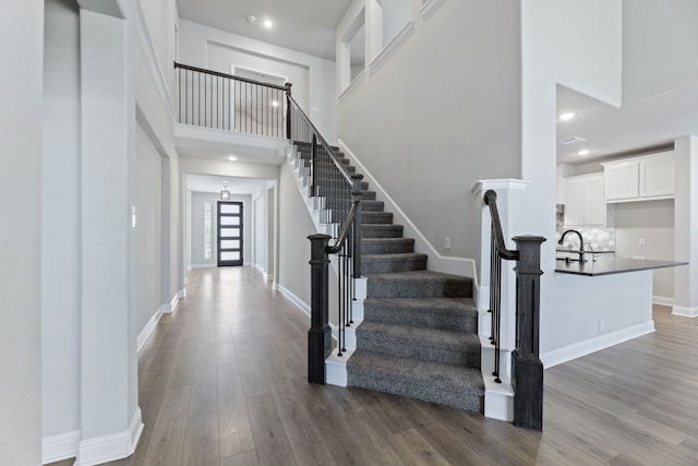 stairway featuring a high ceiling, baseboards, wood finished floors, and recessed lighting