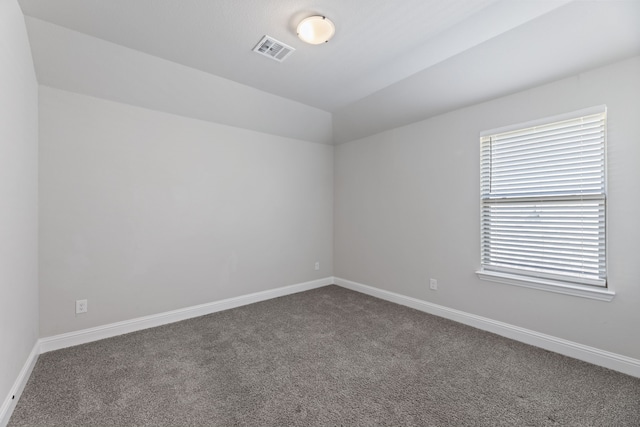 spare room featuring vaulted ceiling, dark carpet, visible vents, and baseboards