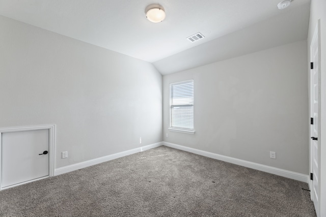 carpeted spare room with visible vents, vaulted ceiling, and baseboards