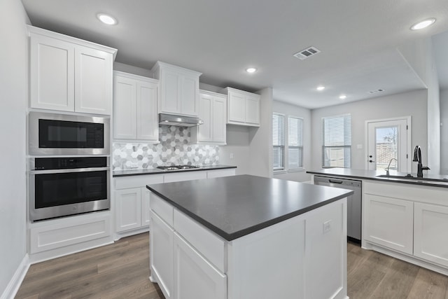 kitchen featuring stainless steel appliances, dark countertops, a sink, and under cabinet range hood