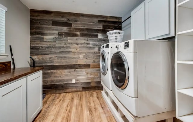 clothes washing area featuring light wood-type flooring, washing machine and dryer, cabinet space, and wooden walls