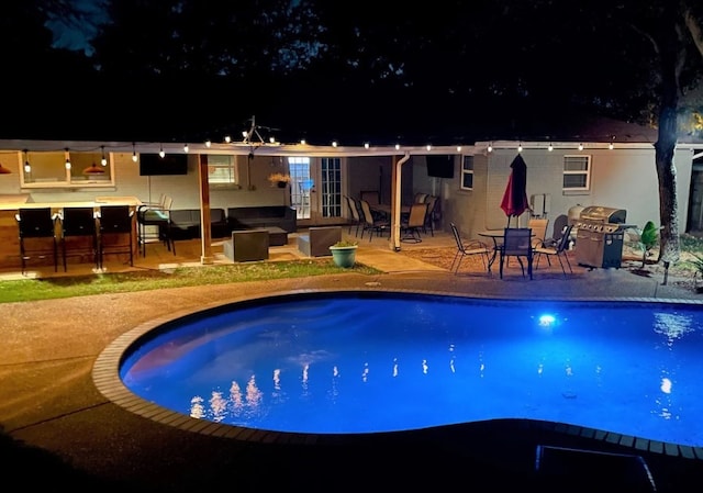 pool at night featuring an outdoor pool, a patio, and grilling area