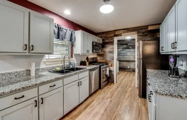 kitchen featuring light wood-style flooring, wood walls, a sink, appliances with stainless steel finishes, and backsplash