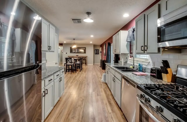 kitchen featuring stainless steel appliances, visible vents, backsplash, light wood-style floors, and a sink