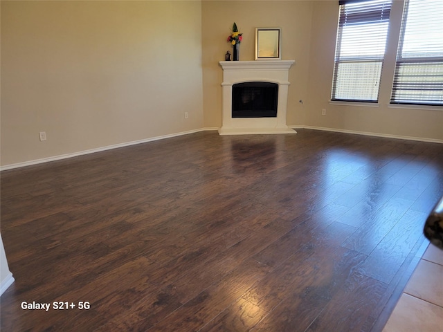 unfurnished living room with dark wood-style floors, a fireplace with raised hearth, and baseboards