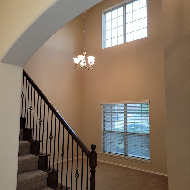 staircase with a notable chandelier, a high ceiling, baseboards, and carpet flooring