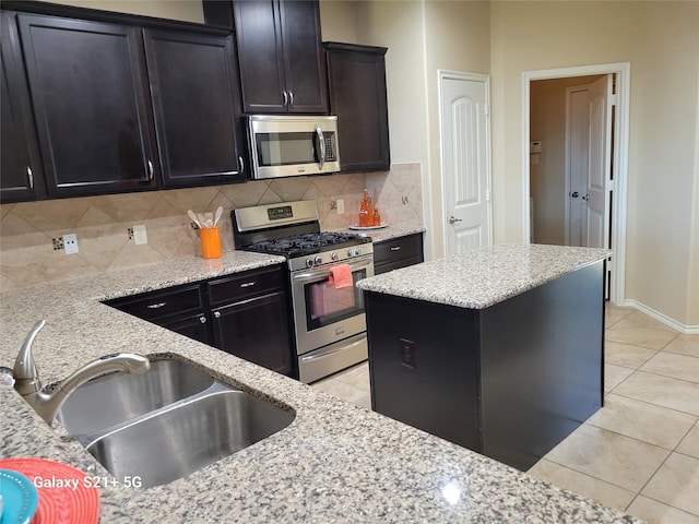 kitchen featuring light tile patterned floors, stainless steel appliances, backsplash, a sink, and light stone countertops