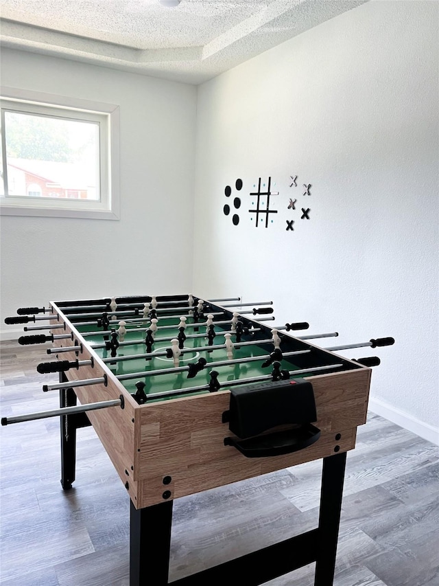 recreation room featuring a textured ceiling, baseboards, and wood finished floors