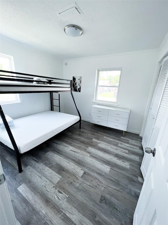 unfurnished bedroom featuring a textured ceiling, ornamental molding, wood finished floors, and baseboards