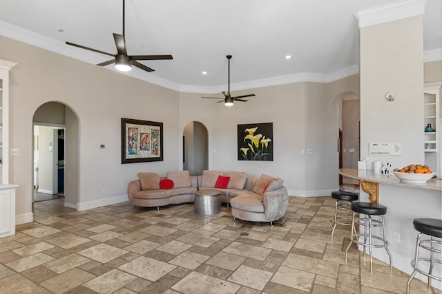 living area featuring stone tile floors, arched walkways, baseboards, ceiling fan, and crown molding