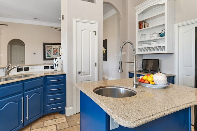 kitchen with arched walkways, stone tile flooring, a sink, and blue cabinetry