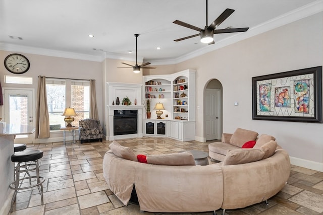 living room featuring arched walkways, baseboards, a glass covered fireplace, and stone tile floors