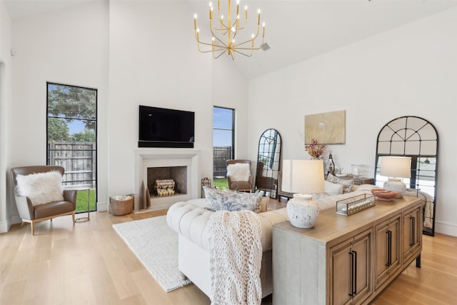 living area with light wood finished floors, a fireplace, high vaulted ceiling, and a notable chandelier