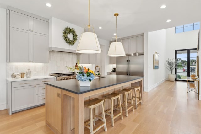 kitchen featuring a kitchen island with sink, light wood-style flooring, stainless steel built in refrigerator, a kitchen breakfast bar, and tasteful backsplash
