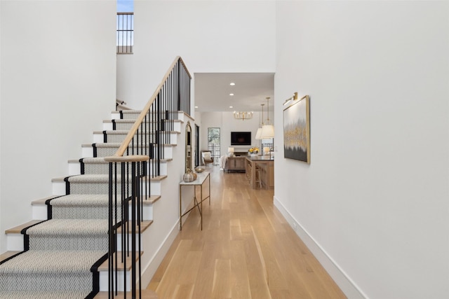 stairs with a towering ceiling, baseboards, wood finished floors, and recessed lighting