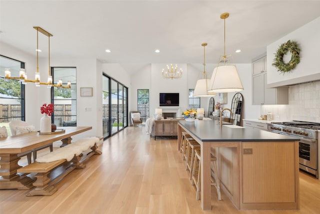 kitchen with light wood finished floors, open floor plan, a notable chandelier, range with two ovens, and an island with sink