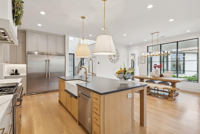 kitchen featuring premium appliances, a sink, a kitchen island with sink, light wood-style flooring, and recessed lighting