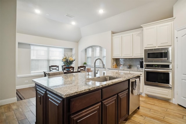 kitchen with backsplash, dark brown cabinetry, appliances with stainless steel finishes, white cabinets, and a sink