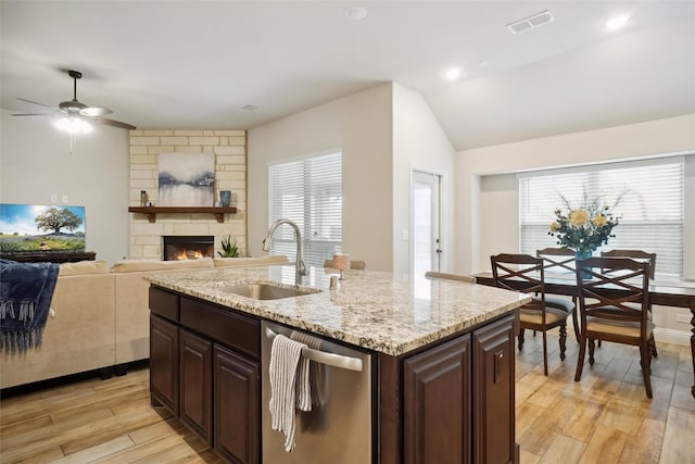 kitchen with a fireplace, a kitchen island with sink, a sink, dishwasher, and light wood-type flooring