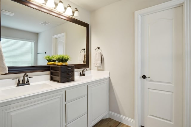 full bath with double vanity, wood finished floors, baseboards, and a sink