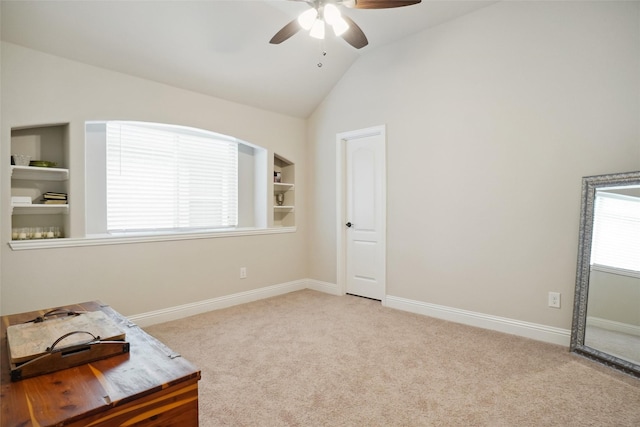 interior space featuring built in shelves, baseboards, carpet, lofted ceiling, and a ceiling fan