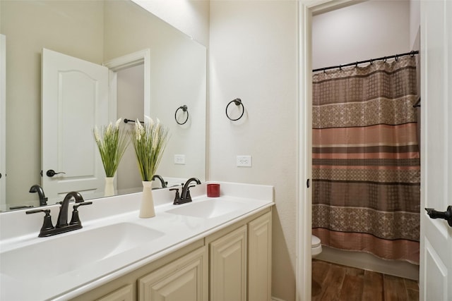 bathroom with double vanity, toilet, wood finished floors, and a sink