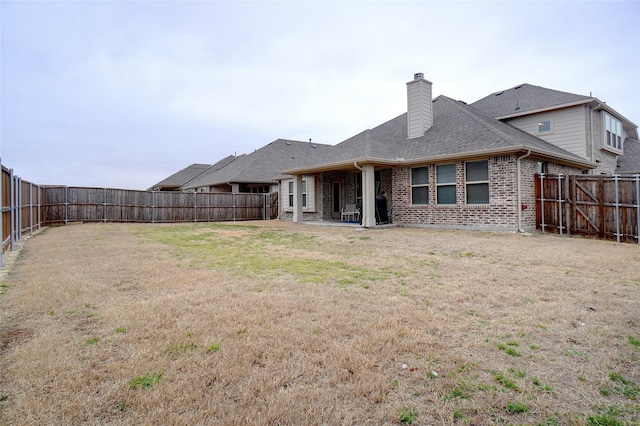 rear view of property with a fenced backyard, a shingled roof, a chimney, a lawn, and brick siding