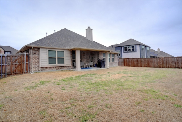 rear view of house with a yard, a patio, brick siding, and a fenced backyard