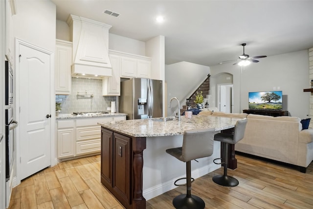 kitchen featuring visible vents, a kitchen bar, custom range hood, light wood-style flooring, and appliances with stainless steel finishes