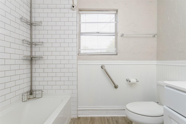 full bathroom featuring toilet, a wainscoted wall, wood finished floors, vanity, and  shower combination